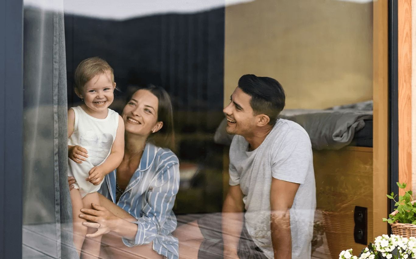 Ein junges und glückliches Ehepaar sitzt mit ihrem Kind am Fenster ihrer Mietwohnung