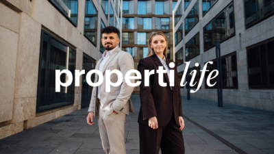 Zwei properti Immobilienmakler stehen zwischen modernen Immobilien und schauen direkt in die Kamera, darüber der Schriftzug propertilife, das Movement fvon properti für Karrieren